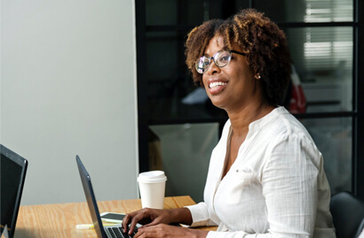A woman is typing on a laptop while looking ahead and smilin