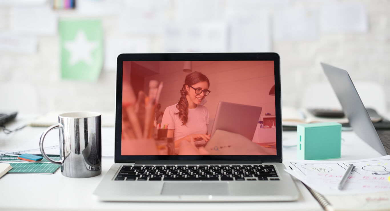 A modern workspace featuring a laptop with a green-tinted screen displaying a woman working